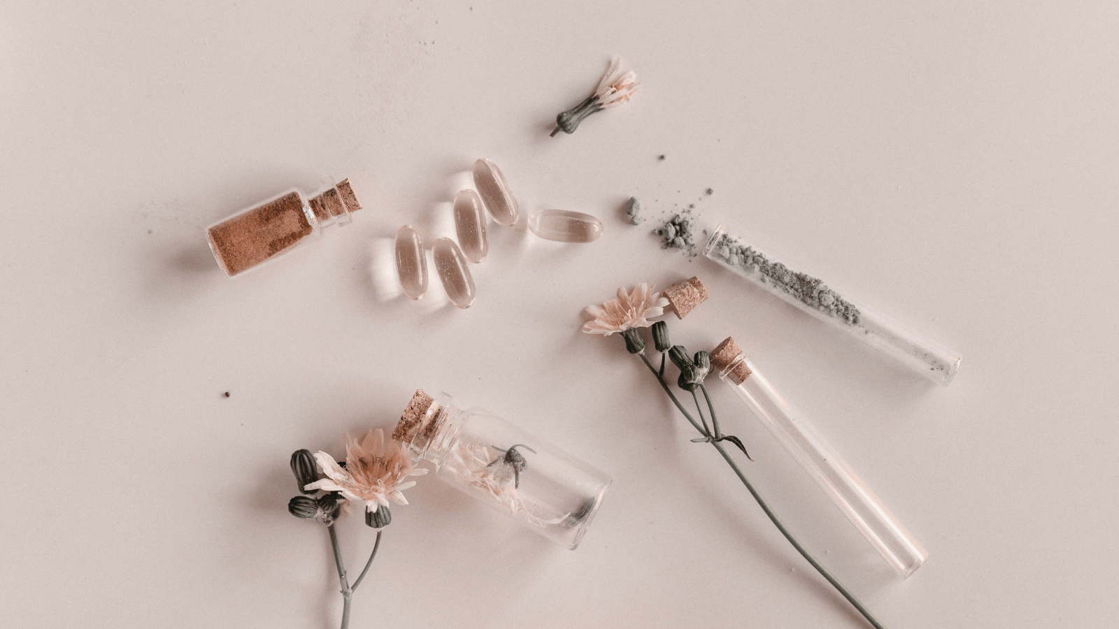 Flat lay of beauty supplements, dried flowers, and powdered ingredients on a blush background—symbolizing daily beauty supplements that actually work.