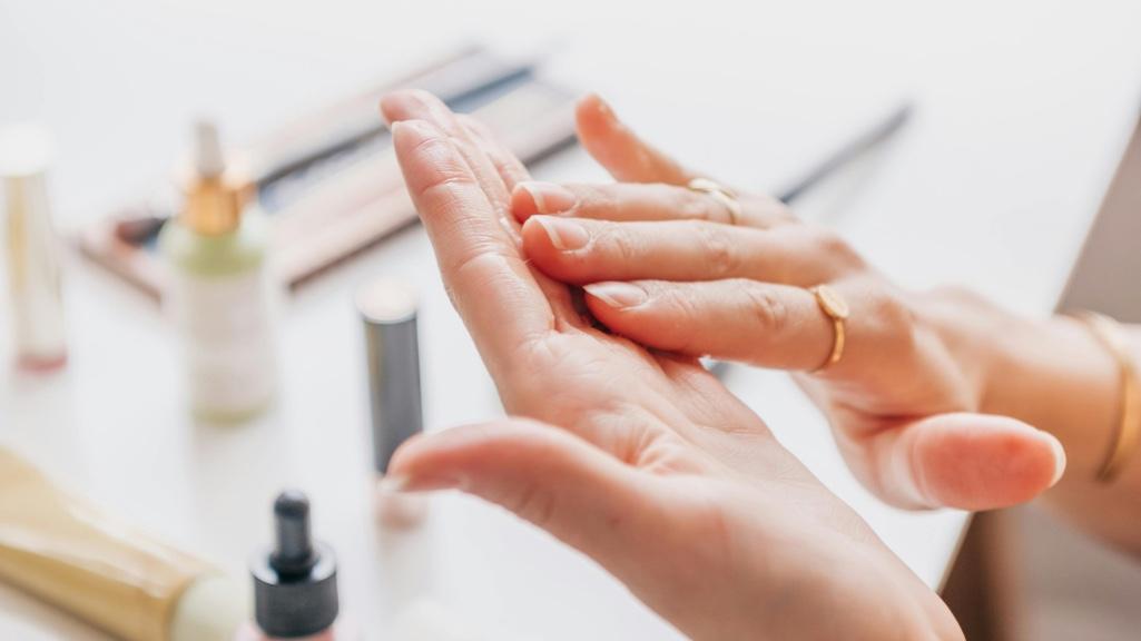 A woman layering skincare products on her hands, with multiple bottles on a neutral background — representing the step-by-step process of layering skincare products properly.
