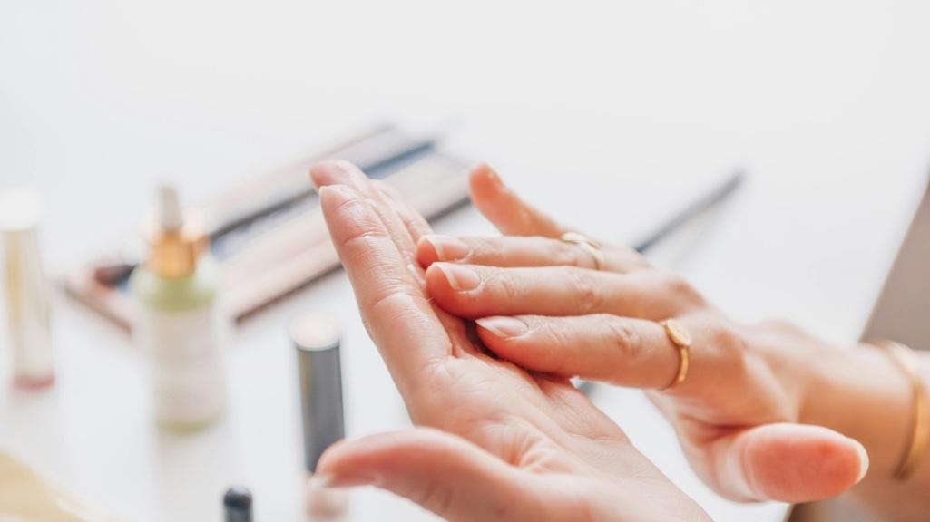 A woman layering skincare products on her hands, with multiple bottles on a neutral background — representing the step-by-step process of layering skincare products properly.