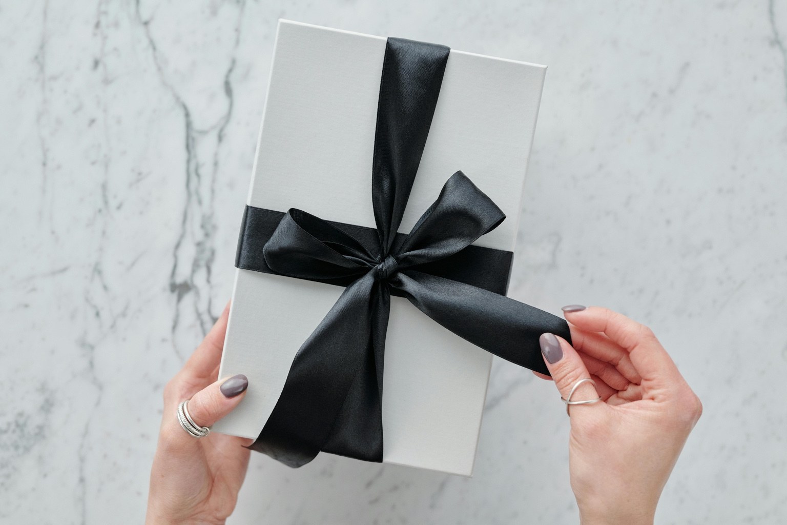 Hands holding a white gift box with black ribbon, representing curated beauty picks