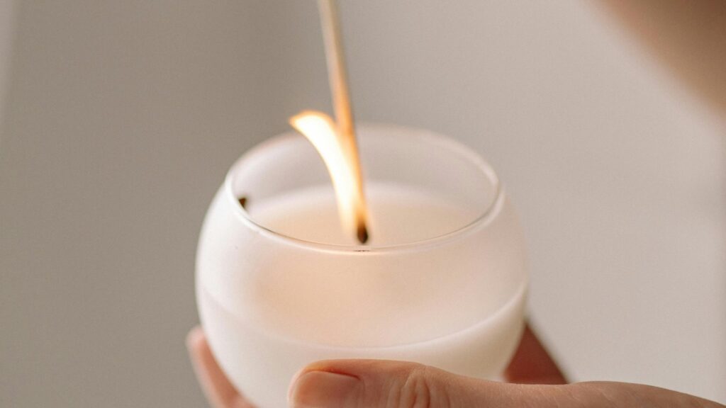 Hand lighting a white candle in soft light, representing calming wellness rituals
