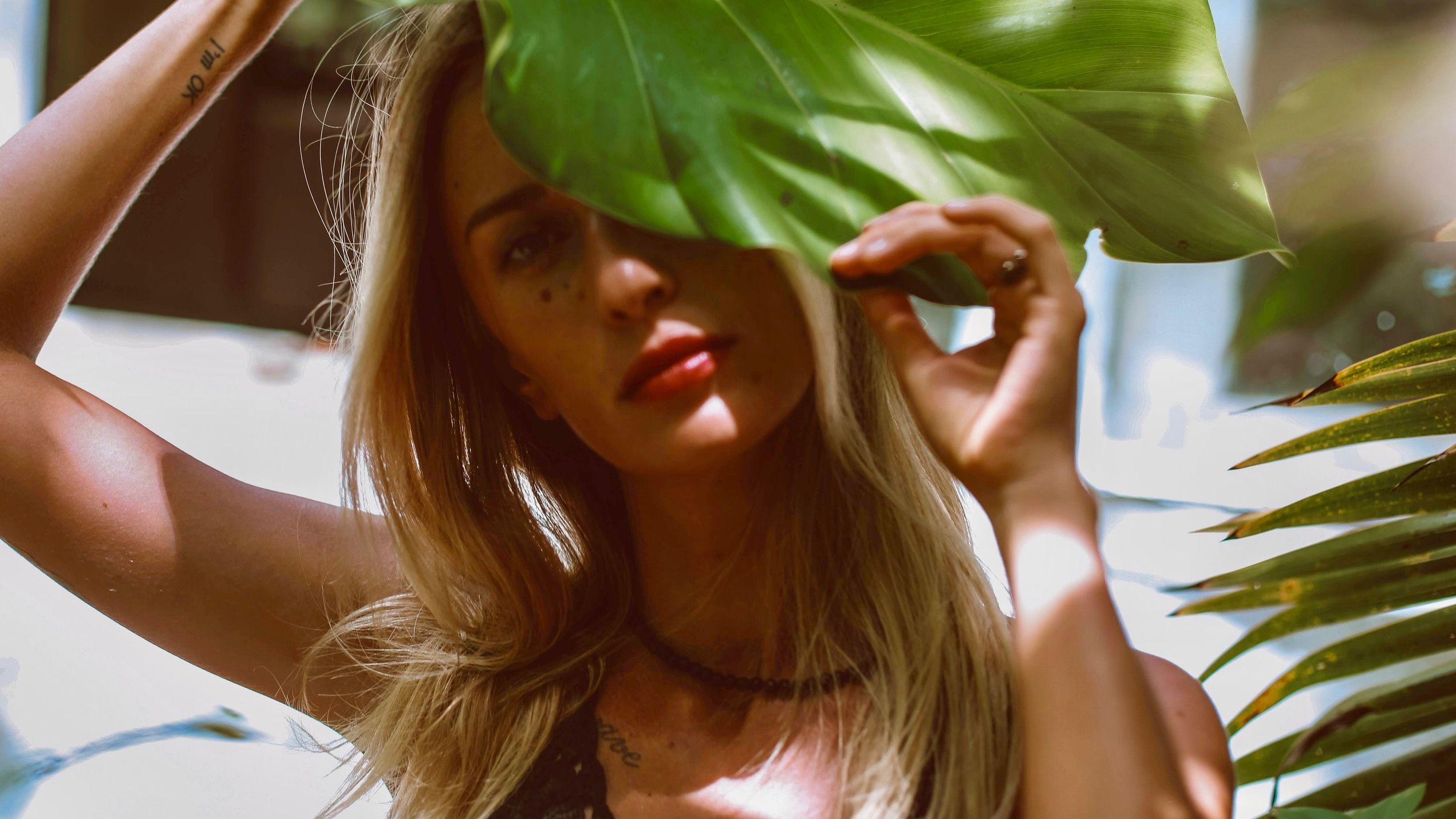Woman's face hiding behind large leaf, subtle notion of transition to fall skincare.