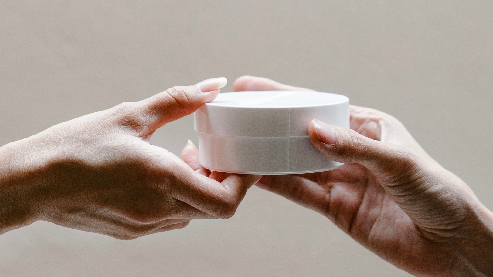 Hands exchanging a skincare jar — representing skin barrier repair routine