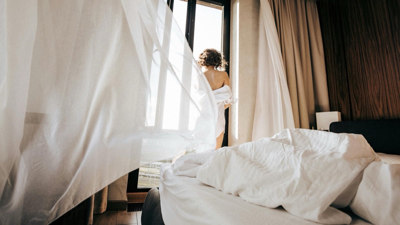 Woman standing at the window with flowing curtains — post for barrier-stressed skin.