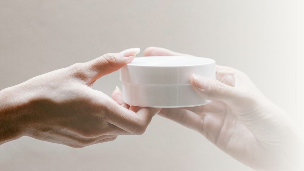 Hands exchanging a skincare jar.