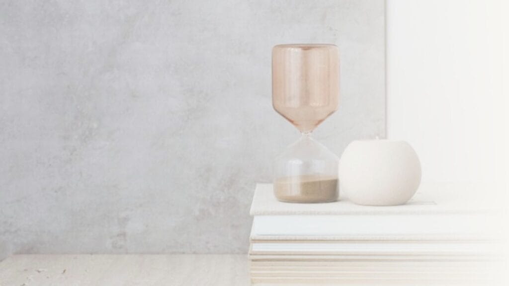 Hourglass on a pile of books with grey background.