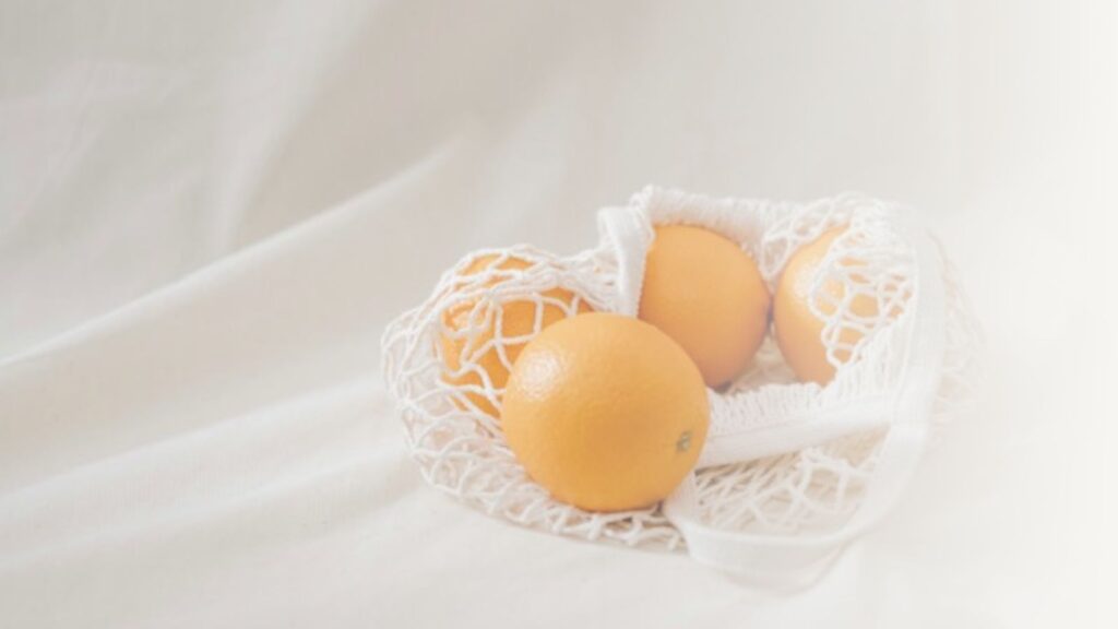 Bag of oranges on grey background.