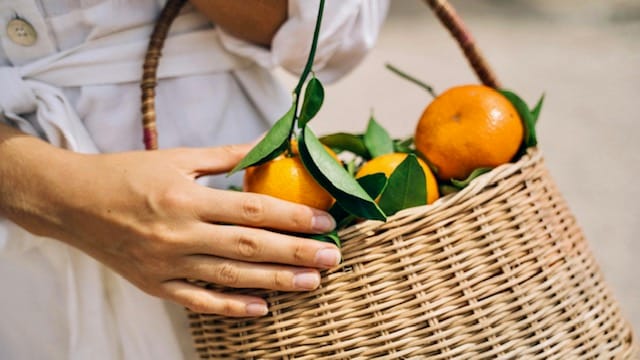 Woman holding a basket with oranges signifying Vitamin C in Skincare