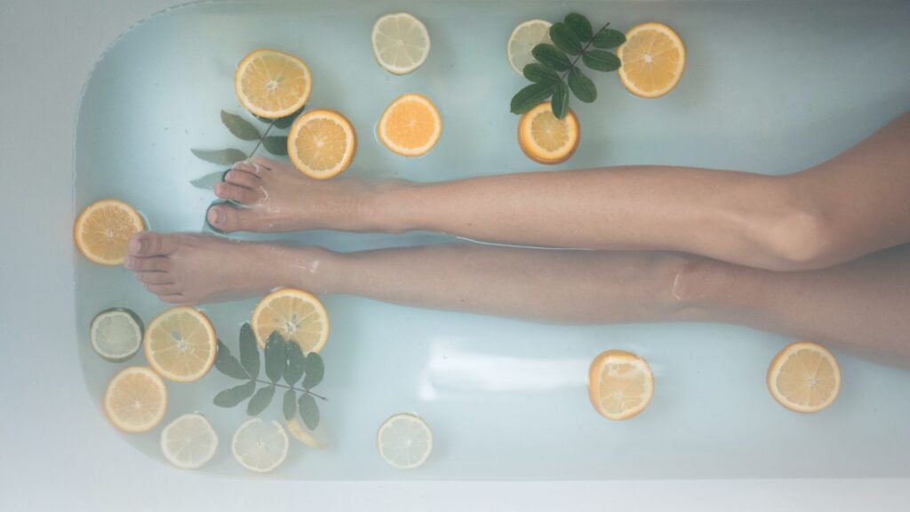 Woman's legs in a bath with floating lemon slices representing vitamin C in skincare