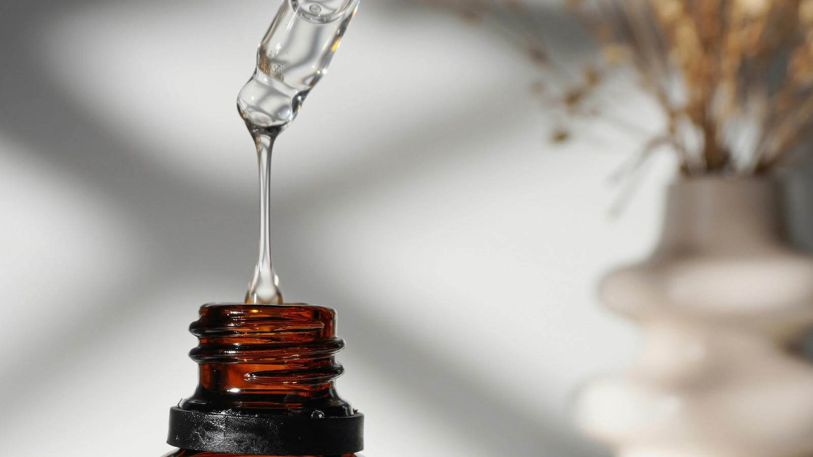 Hydrating serums for dehydrated skin that still feels dry represented by pipette dripping clear water.