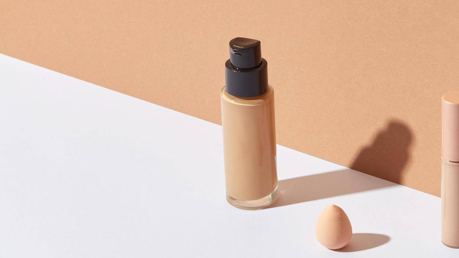 Foundation bottle and makeup sponge on a neutral background, showcasing best dewy foundation.