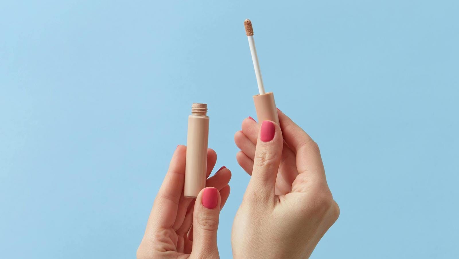 The best concealers for glowing skin illustrated by hands holding concealers against blue background.