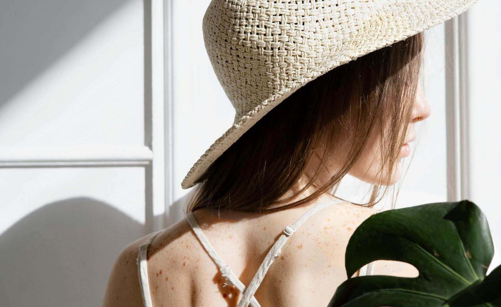 Glow-first picks for heat, humidity, and bare skin days illustrated by woman's sunlit back in summer hat.