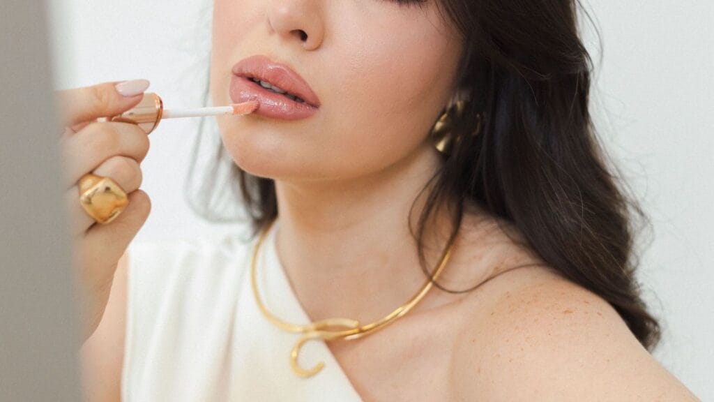 Hybrid makeup formulas behind a softer glow-forward finish illustrated by woman applying hydrating lip gloss.