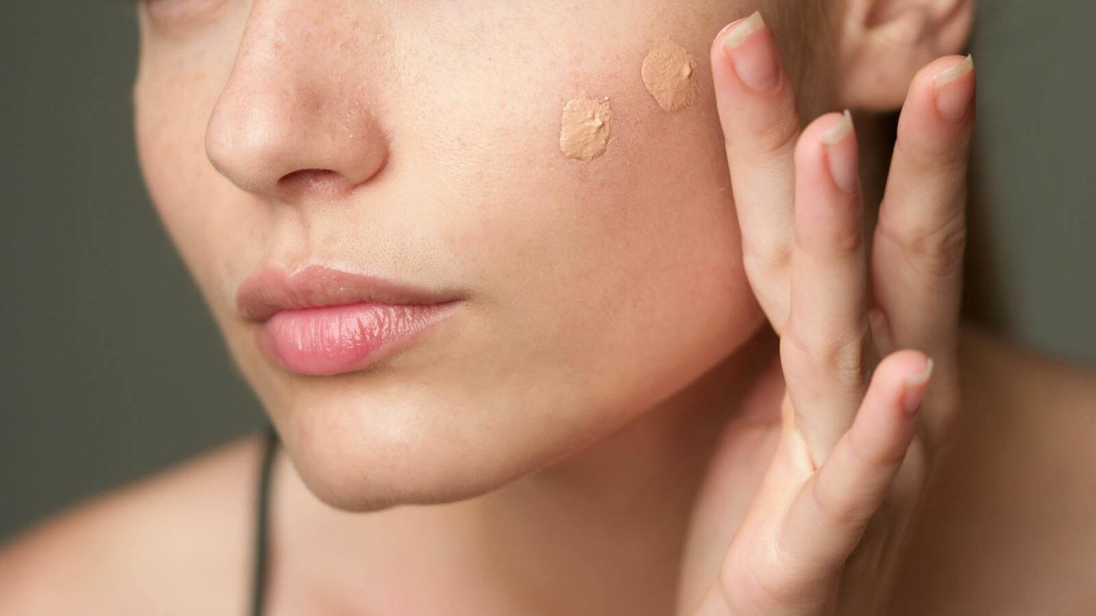 Woman's cheek close up of two makeup dabs illustrating skin tint vs. tinted moisturizer.