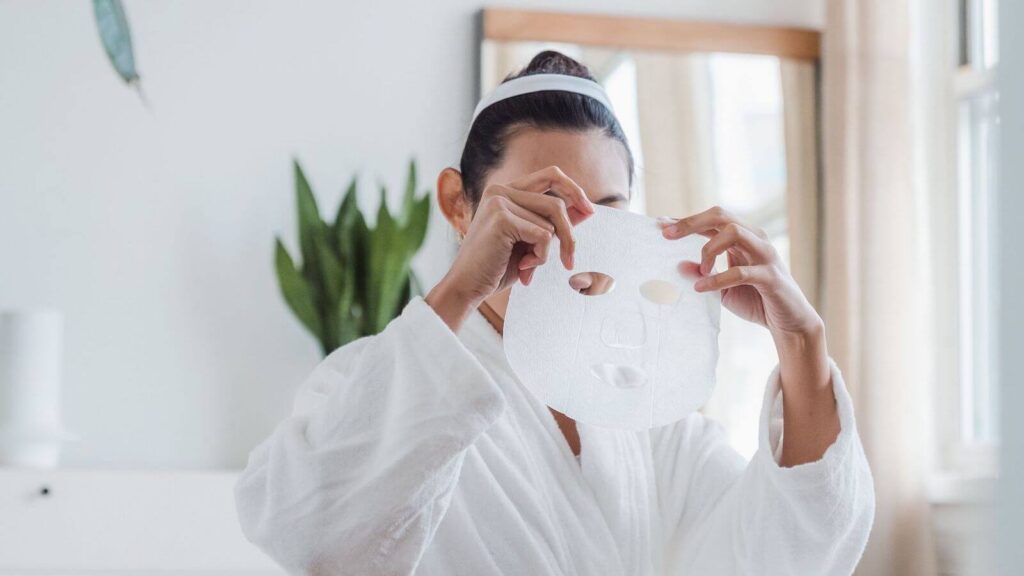 Woman holding a sheet mask as part of a nighttime skincare routine for glowing skin.